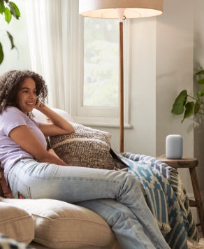 Woman on couch in living room utilizing her Nest Audio Speaker 